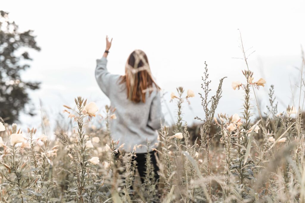 Girl praying through the process with hand up in flower field